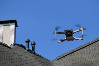 Drone hovering above a tiled roof and chimney inspecting the roofline against a blue sky