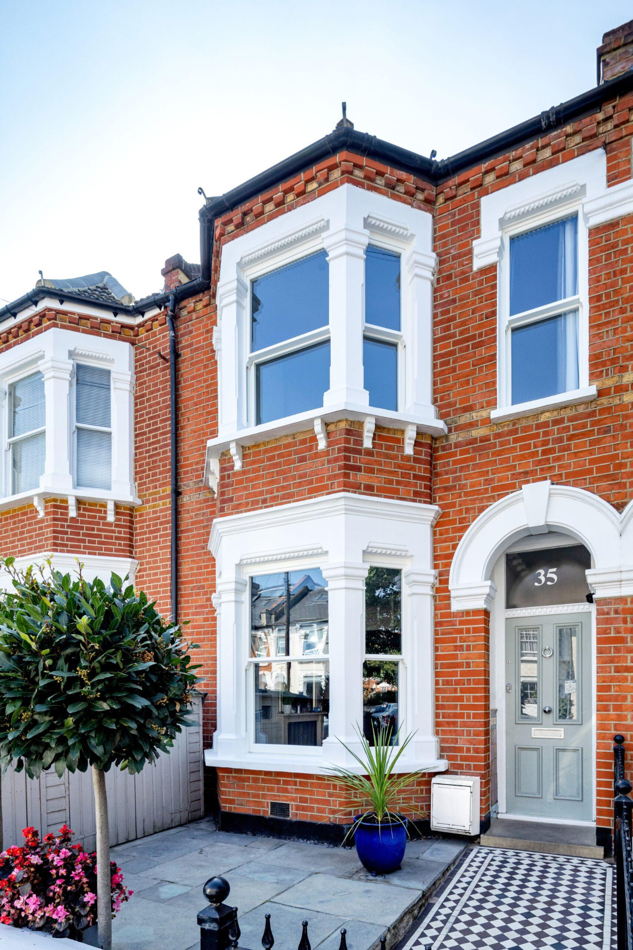 Victorian red brick terraced house with white double bay windows and an arched front door